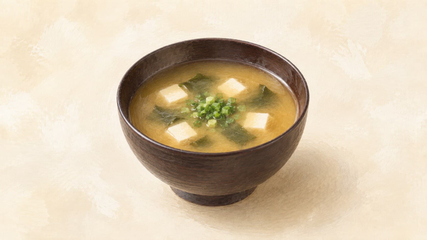A lacquered owan bowl of warm cloudy amber-brown miso soup with silken tofu cubes, wakame, and chopped scallion floating on the surface