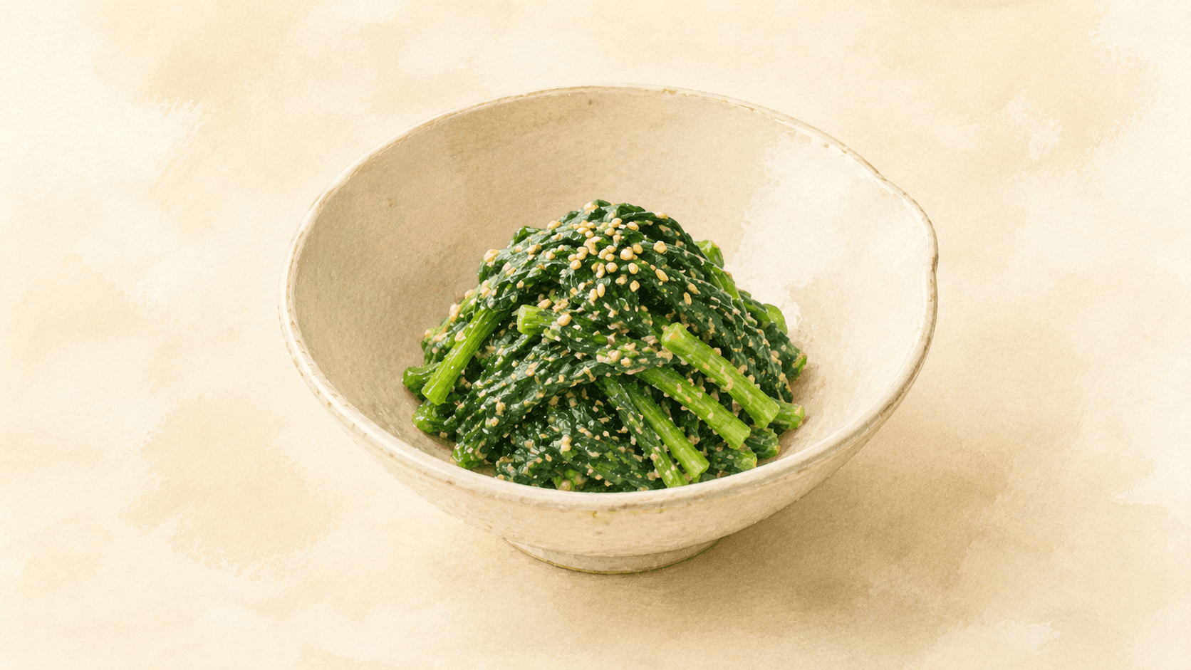 Bright green blanched spinach in a small bowl, coated in a pale sesame dressing with a few whole sesame seeds scattered on top
