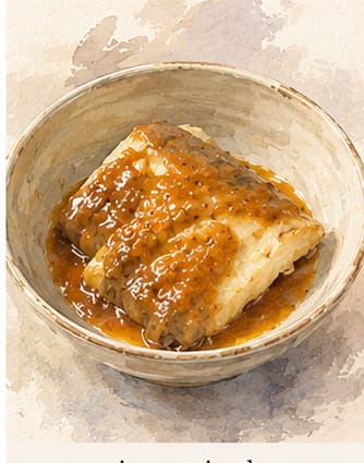 A sablefish fillet in a white miso marinade, resting on a small dish before cooking, with a darker baked version beside it